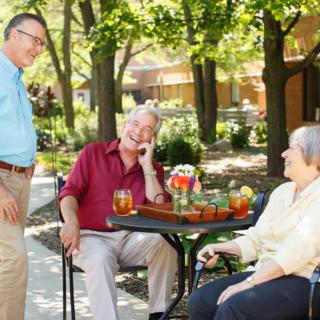 A group of seniors enjoying a conversation outdoors in a garden setting.