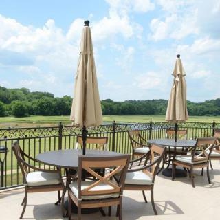 A scenic patio with tables, chairs, and umbrellas overlooking a lush green landscape under a partly cloudy sky.