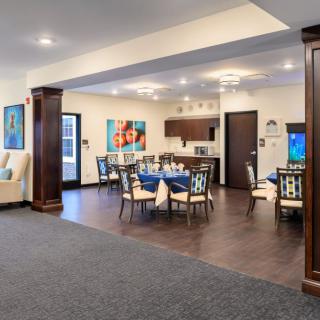 A modern dining area with a kitchen, featuring stylish tables and chairs, enhanced by vibrant artwork and elegant lighting.