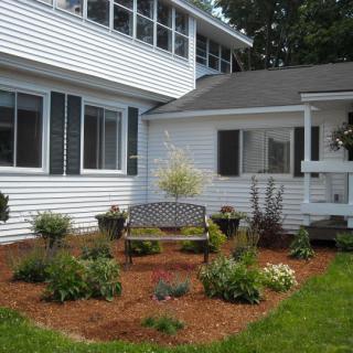 A well-maintained garden with a bench nestled between sections of a white house.
