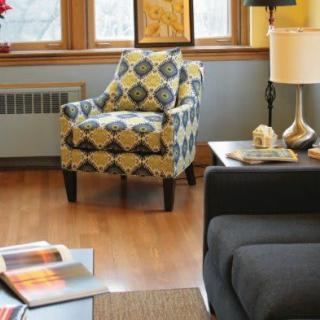 A cozy living room with a patterned armchair, a side table with a lamp, and a dark sofa on hardwood floors.