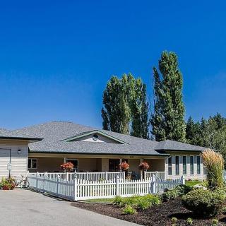 A single-story house with a white fence, surrounded by trees under a clear blue sky.