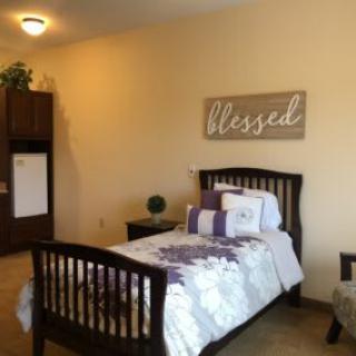 A cozy bedroom with a single bed, featuring decorative pillows and a wall art piece reading 'Blessed'.