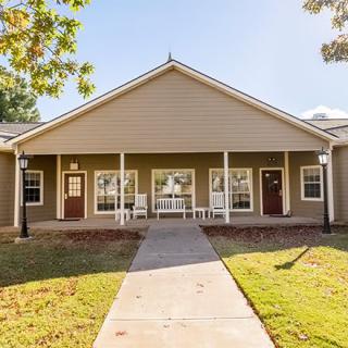 A front view of a residential building with a porch and lawn on a sunny day.