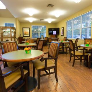 A cozy dining area with several tables and chairs, well-lit by overhead lights and large windows.