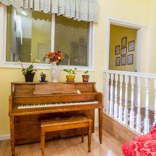 A cozy living room corner with a piano, potted plants, and framed pictures on yellow walls.