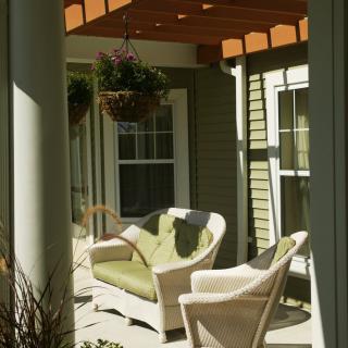 A cozy outdoor patio area featuring wicker furniture under a pergola with hanging plants.
