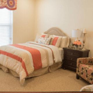 A cozy bedroom with a striped bedspread, nightstand with a lamp, and an accent chair.