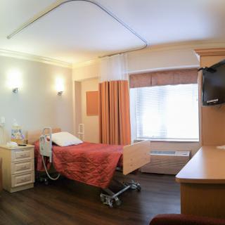 A well-lit hospital patient room with a bed, medical equipment, and a television.