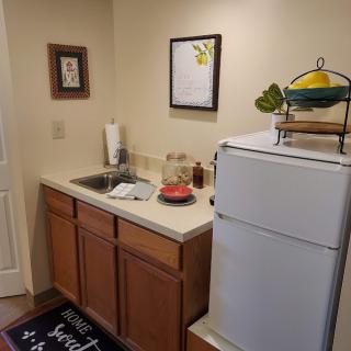 A compact kitchen area with a sink, countertop, and fridge, adorned with home decor and a fruit basket on top.