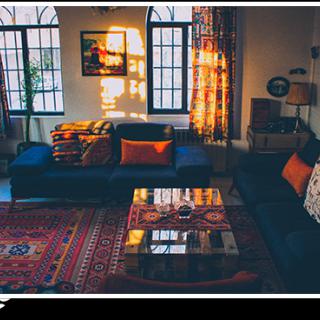 A cozy living room bathed in warm sunset light, featuring a dark sofa with colorful throw pillows, a patterned carpet, and a stylish coffee table.