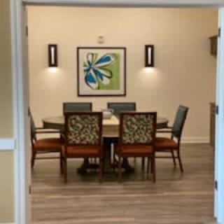 A cozy dining room with a round table, six chairs, decorative artwork, and warm lighting.