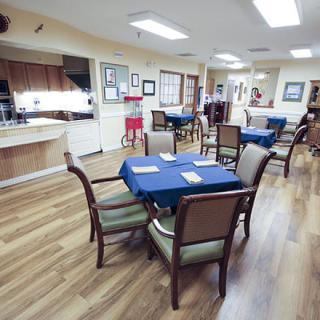 A spacious dining area with tables set for service, featuring blue tablecloths and wooden chairs on a hardwood floor.