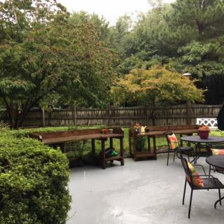 A cozy backyard patio with tables and chairs surrounded by lush greenery.