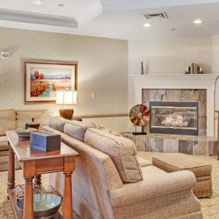 A cozy living room with a comfortable sofa facing a warm fireplace, adorned with artwork and a table lamp.