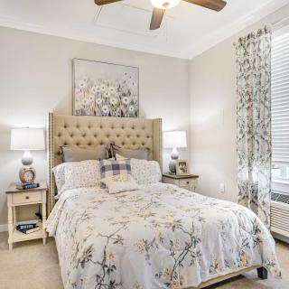 A cozy bedroom with elegant furnishings, featuring a plush bed, matching nightstands with lamps, and decorative artwork above the bed.