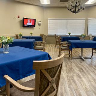 A spacious dining room featuring blue tablecloths, wooden chairs, and a television on the wall.
