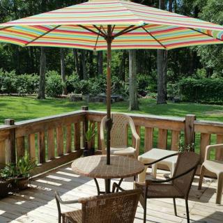 A sunny patio with a table, chairs, and a large striped umbrella overlooking a lush garden.