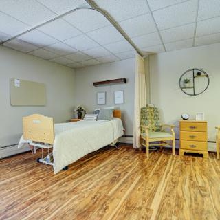 A well-lit and cozy patient room featuring a hospital bed, comfortable chair, and wooden flooring.