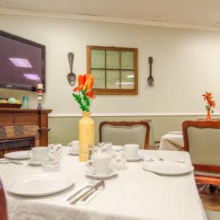 A cozy dining room setup featuring a well-set table, decorative flowers, and a TV in the background.