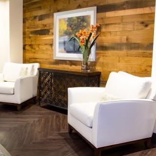 A modern living room with white chairs, a wooden accent wall, and vibrant floral decor.