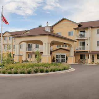 A modern building with a covered entrance and an American flag in front, surrounded by well-maintained landscaping.
