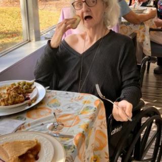 An elderly woman in a wheelchair enjoying a meal indoors.
