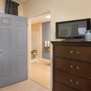 A bedroom with a dresser and television, leading to a bathroom.