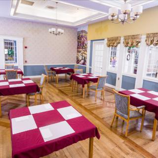 A brightly lit dining room with red and white checkered tablecloths, arranged neatly with chairs around wooden tables.