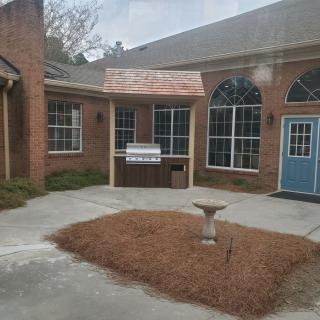 A brick building with large windows and a blue door, featuring a small courtyard with a birdbath.