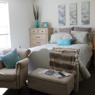 A cozy bedroom with elegant decor, featuring a bed, armchair, dresser, and wall art.
