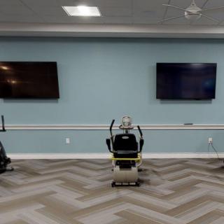 A fitness room with exercise machines and TV screens mounted on the wall.