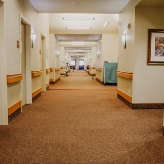 A well-lit hallway with clean, carpeted floors and wooden railings, typical of a hospital or care facility.