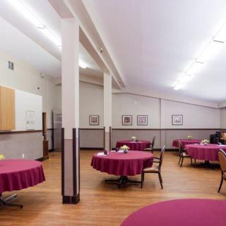 An empty dining room with round tables covered in maroon tablecloths and wooden chairs neatly arranged.