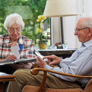 An elderly couple sitting together in a living room, engaged in reading and relaxing.