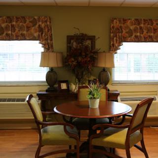 A cozy dining area featuring a round table and comfortable chairs, adorned with decorative curtains and a floral arrangement.