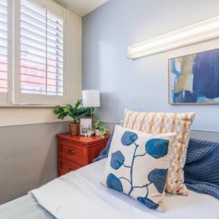 A cozy bedroom with decorative pillows and a bedside table adorned with a lamp and plant.