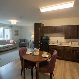 A cozy apartment interior with a combined living room and kitchen, featuring a dining table with two chairs.