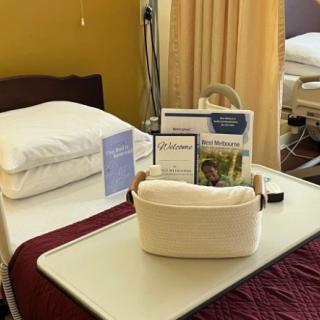 A hospital room with a neatly made bed, adorned with linens and informational pamphlets on a tray table.