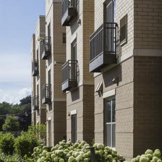 A side view of a modern apartment building with balconies and windows, surrounded by greenery.