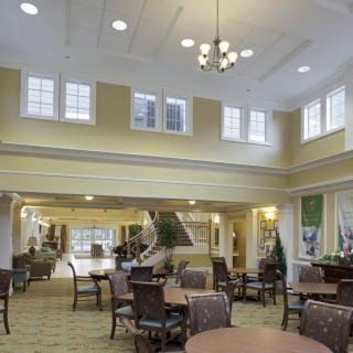 A spacious lobby with seating areas, adorned with tables and chairs, featuring high ceilings and large windows.