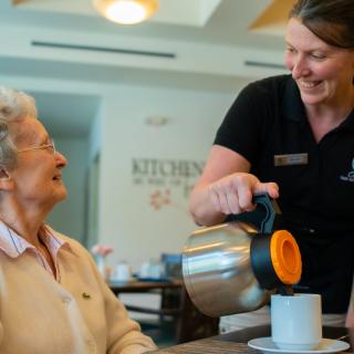 A caregiver pouring tea for an elderly woman, showcasing warmth and care.