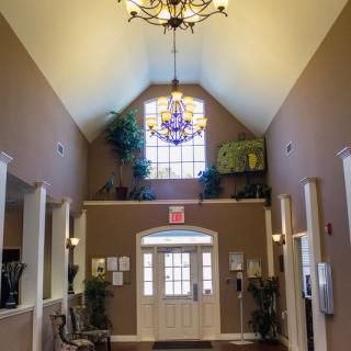 A cozy lobby area with a chandelier and stained glass window, featuring plants and a welcoming atmosphere.