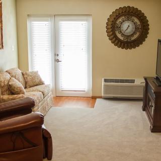 A cozy living room with a sofa, armchair, television, and wall clock.