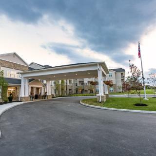 A large building with a prominent entrance and driveway, set against a cloudy sky.