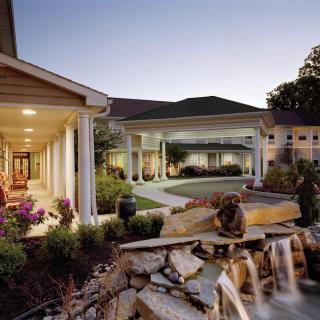 A scenic view of a building with columns, surrounded by a beautifully landscaped garden and a water feature during the evening.