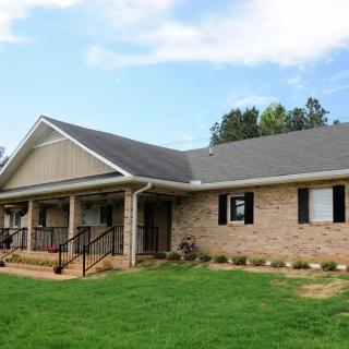 A brick residential house with a porch and a well-maintained lawn.
