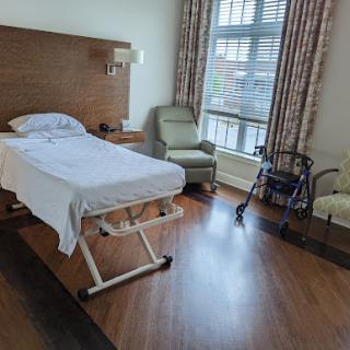 A hospital patient room featuring a bed, a chair, and a walker.