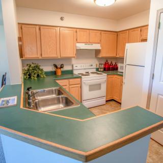 A cozy kitchen with green countertops and wooden cabinets, featuring standard appliances.