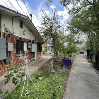 A serene outdoor scene featuring a brick house, garden, and a winding pathway under a clear sky.